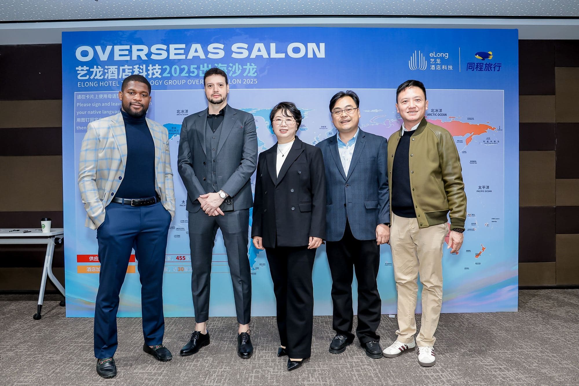 Patrick Che and Jay Dastin with the Elong Hotel Technology Group team in front of the Overseas Salon 2025 board