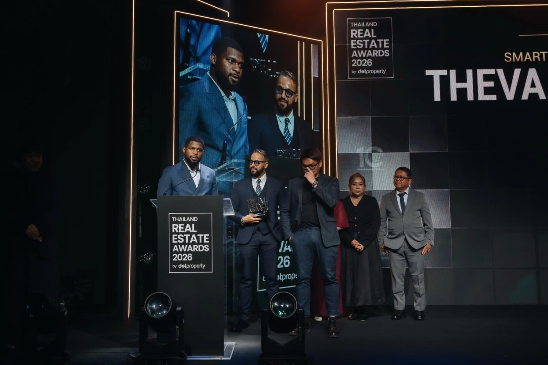 Patrick Che speaking at the lectern on stage at the Thailand Real Estate Awards 2026 with the THEVA team